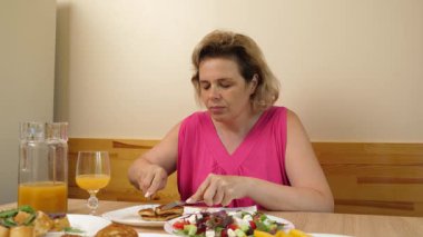 Bir kadın mutfakta masada otururken yiyip içiyor..