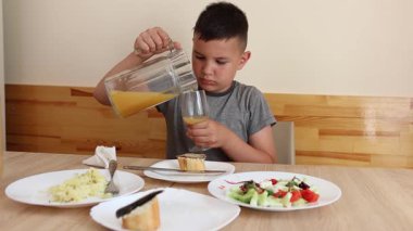 Çocuk masada oturuyor, lezzetli yemekler yiyor ve meyve suyu içiyor..