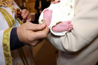 Bir rahip vaftiz sırasında bebek ayaklarını kutsal yağla yağlar. Yetişkin biri tarafından tutulan beyaz giysili bebek..