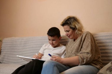 Anne ve oğlu kanepede otururken beyaz tahtaya resim çiziyorlar..