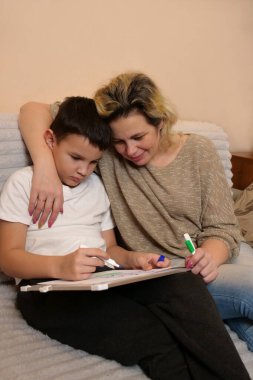 Anne ve oğlu kanepede otururken beyaz tahtaya resim çiziyorlar..
