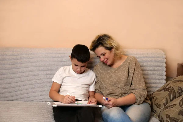 Anne ve oğlu kanepede otururken beyaz tahtaya resim çiziyorlar..