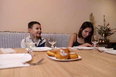 Erkek ve kız kardeş Noel ağacının olduğu bir odaya sofra, tabak, çatal bıçak takımı ve peçeteler kurdular. Ilık ışıklandırma ve yumuşak odaklanma sıcak bir aile ortamı yaratır..