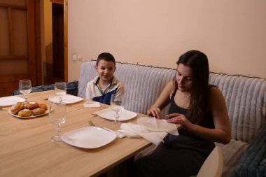 Erkek ve kız kardeş Noel ağacının olduğu bir odaya sofra, tabak, çatal bıçak takımı ve peçeteler kurdular. Ilık ışıklandırma ve yumuşak odaklanma sıcak bir aile ortamı yaratır..