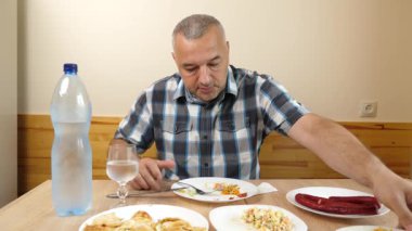 Adam mutfak masasında otururken su içip yemek yiyor.