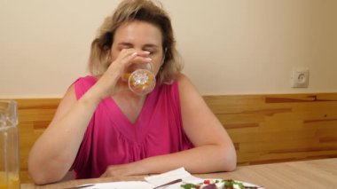 Bir kadın mutfakta masada otururken yiyip içiyor..