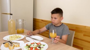 Çocuk masada oturuyor, lezzetli yemekler yiyor ve meyve suyu içiyor..