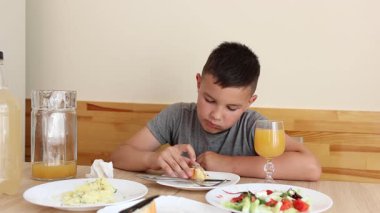 Çocuk masada oturuyor, lezzetli yemekler yiyor ve meyve suyu içiyor..