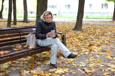 Bir kadın, güzel bir sonbahar gününde parkta bir bankta otururken telefonla konuşuyor..