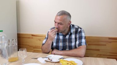 Bir adam mutfakta masada oturuyor, yiyor ve içiyor..