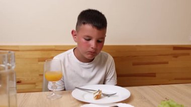 Bir çocuk masada otururken meyve suyu yer ve içer..