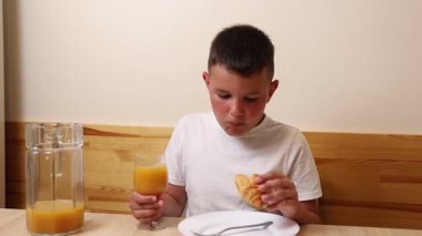 Bir çocuk masada otururken meyve suyu yer ve içer..