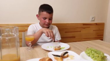 Bir çocuk masada otururken meyve suyu yer ve içer..