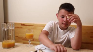 Bir çocuk masada otururken meyve suyu yer ve içer..