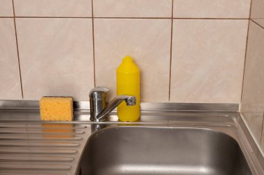 Mutfak lavabosu metal musluk, sarı sünger ve plastik şişe döşeme duvarına karşı deterjan için..