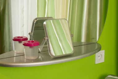 Duvardaki aynanın önündeki masa aynasında pembe kapağı ve yansıması olan plastik bir kap var..