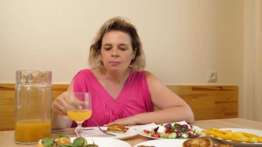 Bir kadın mutfakta masada otururken yiyip içiyor..