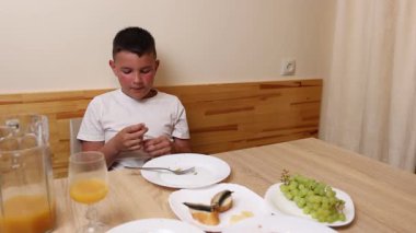 Bir çocuk masada otururken meyve suyu yer ve içer..