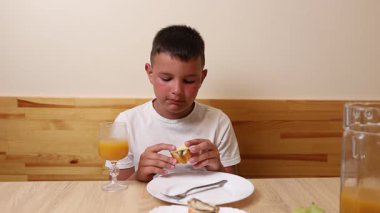 Bir çocuk masada otururken meyve suyu yer ve içer..