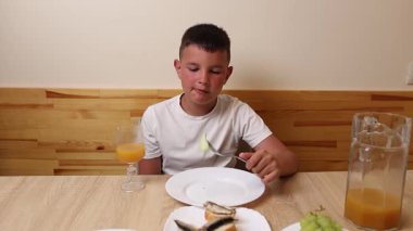 Bir çocuk masada otururken meyve suyu yer ve içer..