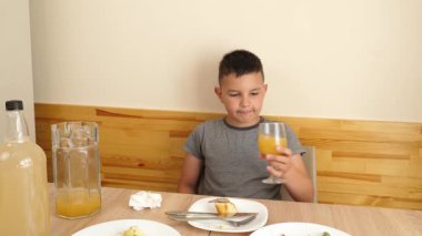 Çocuk masada oturuyor, lezzetli yemekler yiyor ve meyve suyu içiyor..