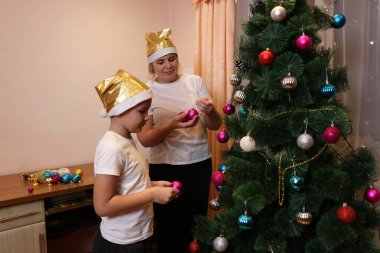 Anne ve çocuk odada bir Noel ağacı süsler, altın şapkalar takar, rahat bir şenlik ortamı hazırlarlar..