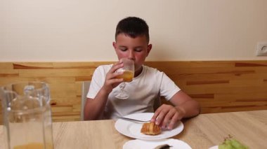 Bir çocuk masada otururken meyve suyu yer ve içer..