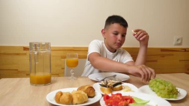 Bir çocuk masada otururken meyve suyu yer ve içer..