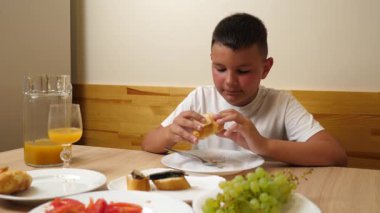 Bir çocuk masada otururken meyve suyu yer ve içer..