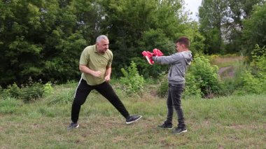 Çocuk, Green Park 'ta yetişkin koçuyla boks antrenmanı yapıyor..