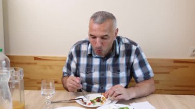 Bir adam mutfakta masada oturuyor, yiyor ve içiyor..