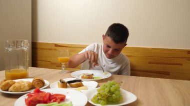 Bir çocuk masada otururken meyve suyu yer ve içer..