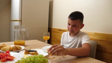 Bir çocuk masada otururken meyve suyu yer ve içer..