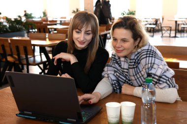 İki kadın bir kafede masada otururken dizüstü bilgisayarda çalışıyor.