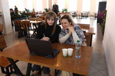 İki kadın bir kafede masada otururken dizüstü bilgisayarda çalışıyor.