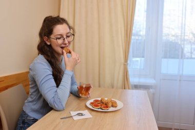 Bir kadın kahvaltıda çay içer ve hamur işi yer..