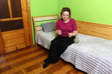 Bir kadın kanepede otururken yün iplik çevirir..