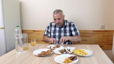 Bir adam mutfakta masada oturuyor, yiyor ve içiyor..