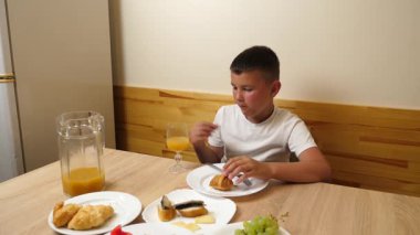 Bir çocuk masada otururken meyve suyu yer ve içer..