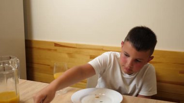 Bir çocuk masada otururken meyve suyu yer ve içer..