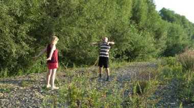 Güneşli bir yaz gününde, iki kişi, yeşil bir nehir kenarında, kayalık bir yerde sabah egzersizleri yapıyor..