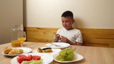 Bir çocuk masada otururken meyve suyu yer ve içer..