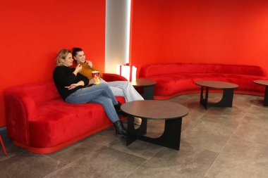 İki kadın kanepede oturmuş film beklerken patlamış mısır yiyorlar..