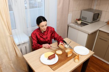 Kadın mutfak masasında otururken sandviç yapıyor.