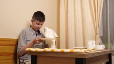 Bir adam mutfakta masada otururken bulaşıkları yıkayıp parlatıyor..