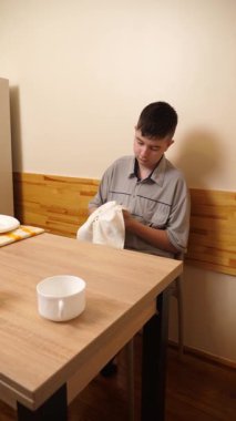 Bir adam mutfakta masada otururken bulaşıkları yıkayıp parlatıyor..