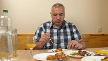 Adam mutfak masasında otururken su içip yemek yiyor.