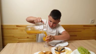 Bir çocuk masada otururken meyve suyu yer ve içer..