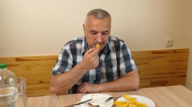 Adam mutfak masasında otururken su içip yemek yiyor.