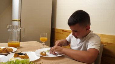 Bir çocuk masada otururken meyve suyu yer ve içer..